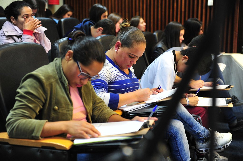 Alunos em cursinho preparatório estudando para concursos públicos e fazendo anotações em sala de aula.