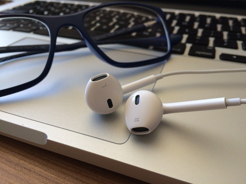 Fones de ouvido brancos e óculos sobre o teclado de um notebook